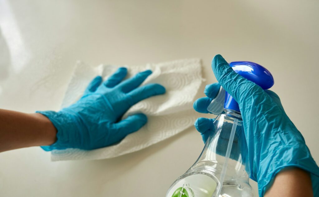 A person wearing blue gloves uses a spray bottle and paper towel to clean a surface, demonstrating Ryak Cleaning's commitment to pristine results in Belfast.