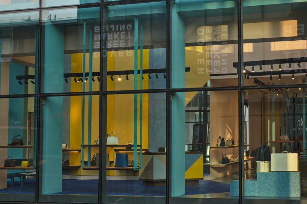 A storefront window, meticulously maintained by Professional Window Cleaning, showcases various handbags and accessories inside a modern retail store with teal and yellow interior decor.