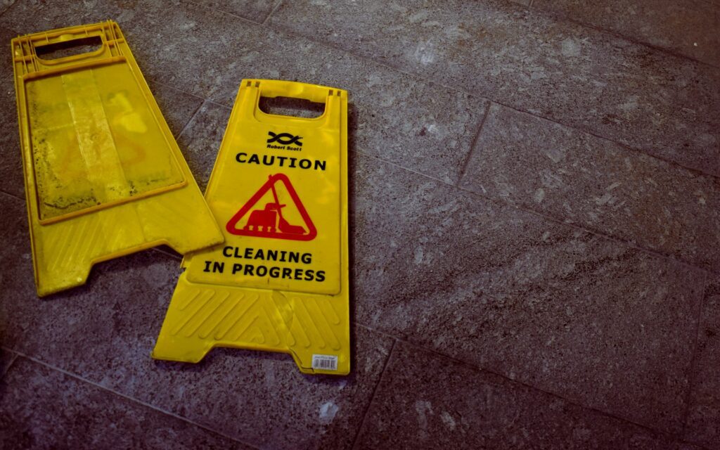 Two yellow caution signs that read "CAUTION CLEANING IN PROGRESS" lie on a tiled floor.