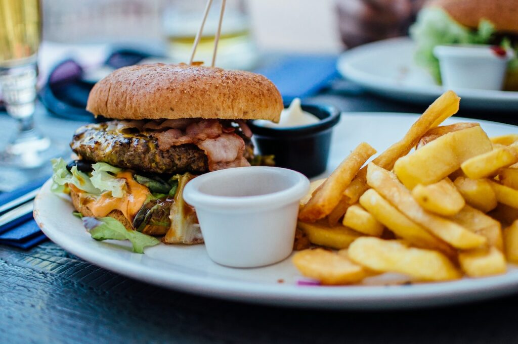 A plate with a bacon cheeseburger, a side of fries, and small containers of sauce on a table.