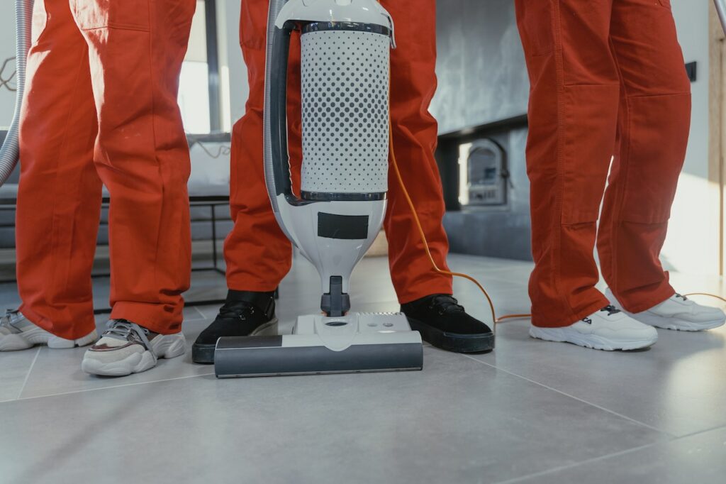 Three people in red overalls stand beside a vacuum cleaner on a tiled floor, showcasing the advantages of professional cleaning services.