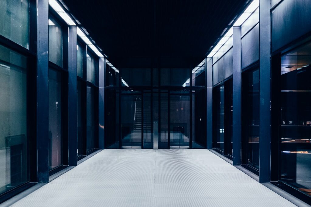 A modern, dimly lit hallway with large glass panels and a staircase at the end.